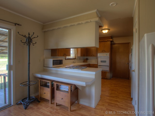 kitchen featuring a kitchen breakfast bar, kitchen peninsula, light hardwood / wood-style flooring, and white appliances