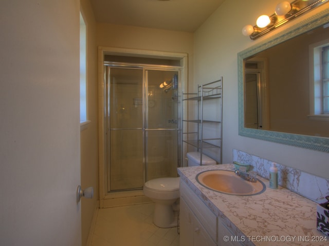 bathroom with tile patterned flooring, vanity, a shower with shower door, and toilet