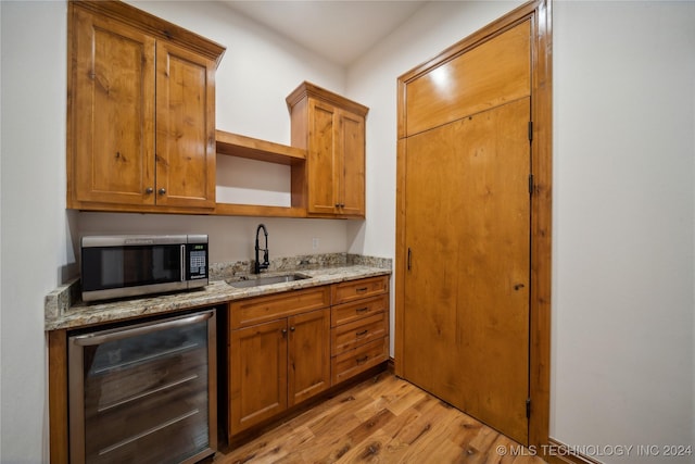 kitchen featuring light stone countertops, beverage cooler, light hardwood / wood-style flooring, and sink