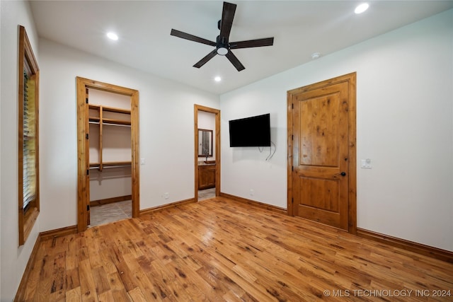 unfurnished bedroom featuring a walk in closet, a closet, light wood-type flooring, ceiling fan, and ensuite bathroom