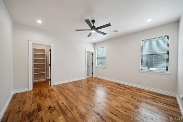 unfurnished bedroom with ceiling fan, a walk in closet, a closet, and hardwood / wood-style floors