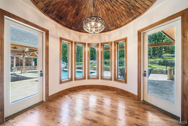 doorway with lofted ceiling, brick ceiling, a chandelier, and light hardwood / wood-style floors