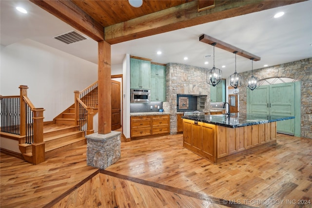 kitchen featuring light wood-type flooring, a kitchen island with sink, beamed ceiling, and pendant lighting