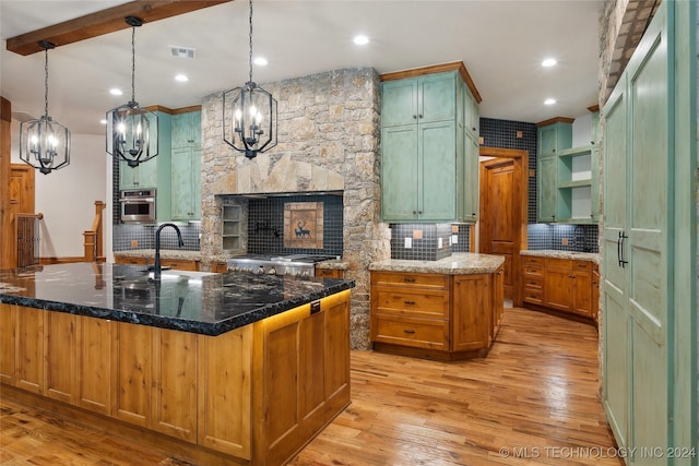 kitchen featuring appliances with stainless steel finishes, light hardwood / wood-style flooring, a center island with sink, and dark stone counters