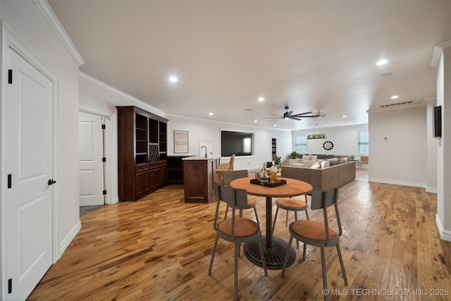 dining room with light wood-type flooring, ceiling fan, and crown molding