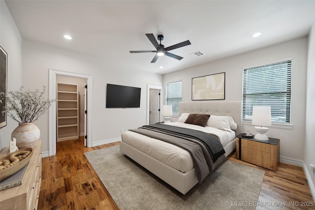 bedroom featuring a spacious closet, dark wood-type flooring, a closet, and ceiling fan