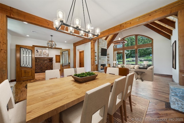 dining space with wood-type flooring, a stone fireplace, a notable chandelier, high vaulted ceiling, and beam ceiling