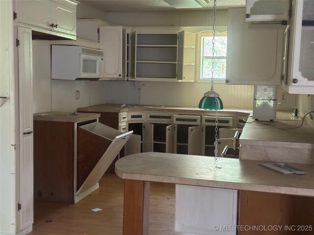 26385 State Highway 1 E, Allen, OK 74825 - kitchen with wood finished floors, white cabinets, white microwave, and decorative light fixtures