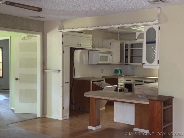 26385 State Highway 1 E, Allen, OK 74825 - kitchen featuring white microwave, wood finished floors, a peninsula, and a textured ceiling