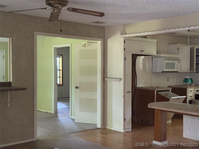 26385 State Highway 1 E, Allen, OK 74825 - kitchen with white microwave, ceiling fan, a textured ceiling, wood finished floors, and baseboards