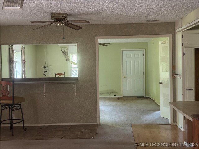 26385 State Highway 1 E, Allen, OK 74825 - kitchen featuring ceiling fan, a textured ceiling, a breakfast bar, carpet, and baseboards