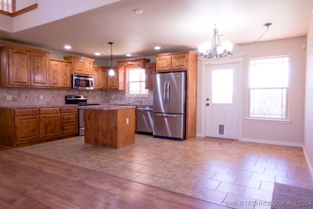 kitchen with a healthy amount of sunlight, a kitchen island, hanging light fixtures, and appliances with stainless steel finishes