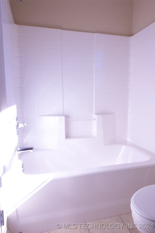 bathroom featuring tile patterned floors, toilet, and a tub to relax in