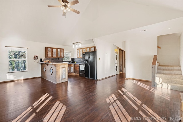 unfurnished living room featuring ceiling fan, dark hardwood / wood-style flooring, stacked washing maching and dryer, and high vaulted ceiling