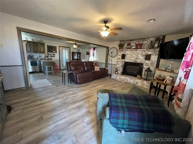 living room with a wood stove, ceiling fan, wood-type flooring, and a textured ceiling