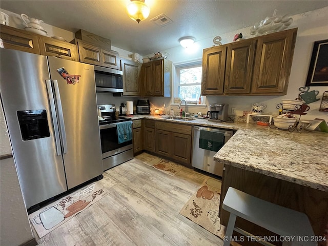 kitchen featuring sink, light stone countertops, a textured ceiling, light wood-type flooring, and appliances with stainless steel finishes