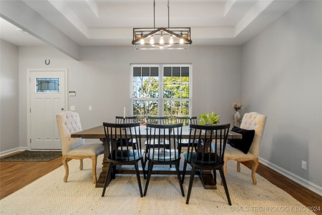 dining room with hardwood / wood-style flooring, a notable chandelier, and a raised ceiling