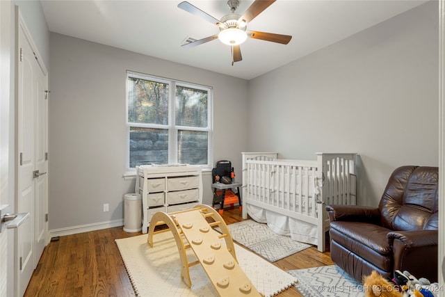 bedroom featuring ceiling fan, dark hardwood / wood-style flooring, and a nursery area