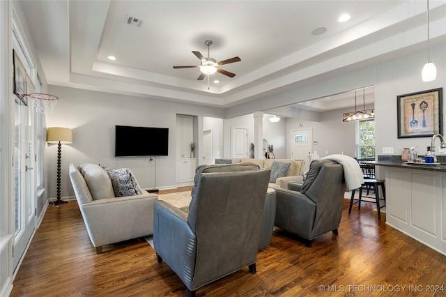 living room with dark hardwood / wood-style floors, a raised ceiling, ceiling fan, and decorative columns