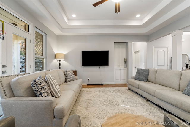 living room with a tray ceiling, ceiling fan, decorative columns, and light wood-type flooring