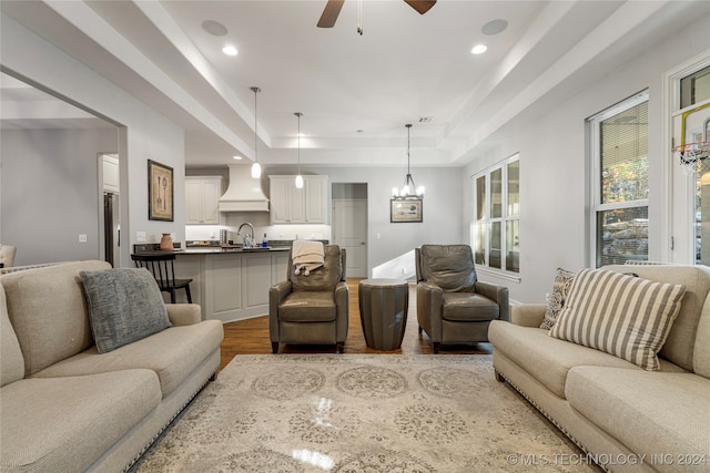 living room with a tray ceiling, sink, light hardwood / wood-style floors, and ceiling fan with notable chandelier