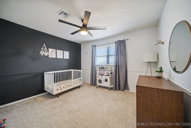 carpeted bedroom featuring ceiling fan, a nursery area, and a textured ceiling