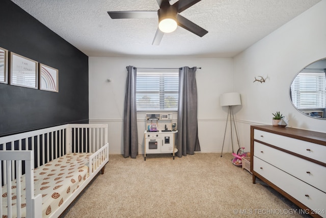 carpeted bedroom with a crib, a textured ceiling, and ceiling fan