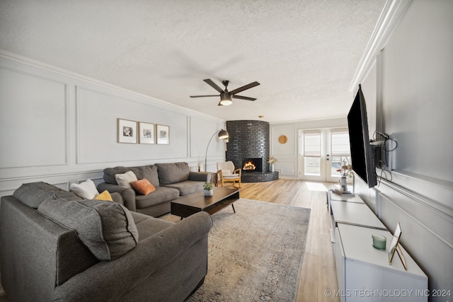 living room with a textured ceiling, light hardwood / wood-style floors, ceiling fan, a brick fireplace, and crown molding