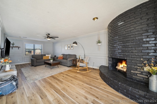 living room with ceiling fan, hardwood / wood-style flooring, a brick fireplace, and ornamental molding