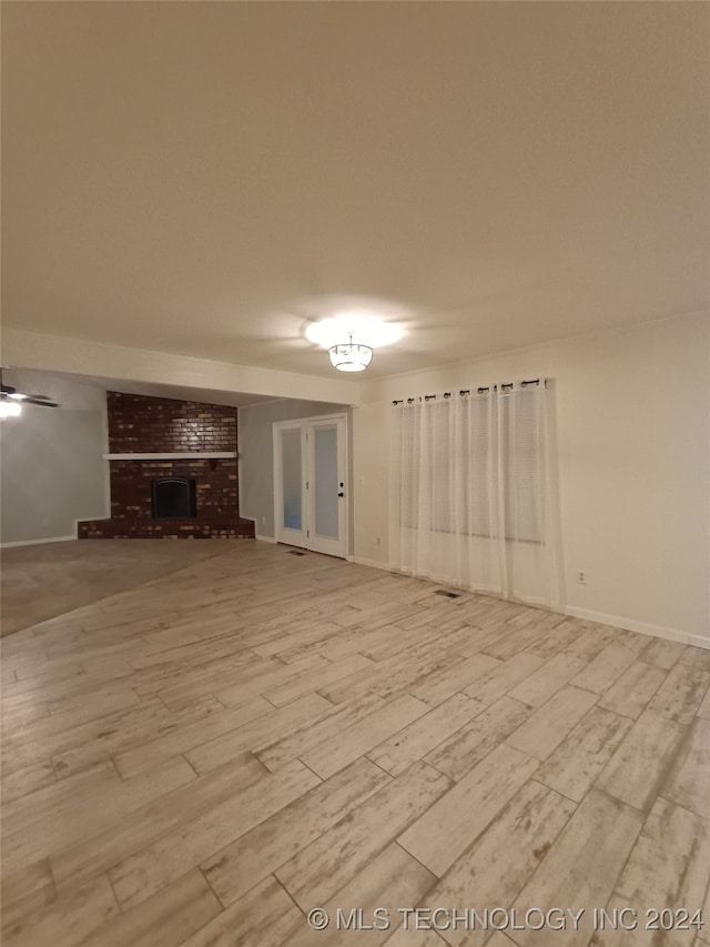 unfurnished living room featuring ceiling fan, light hardwood / wood-style floors, and a brick fireplace