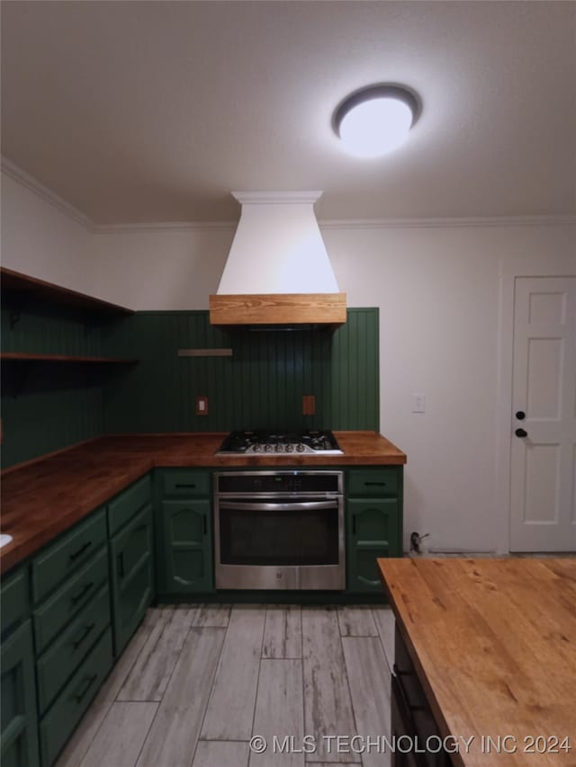 kitchen with wood counters, custom exhaust hood, green cabinetry, ornamental molding, and appliances with stainless steel finishes