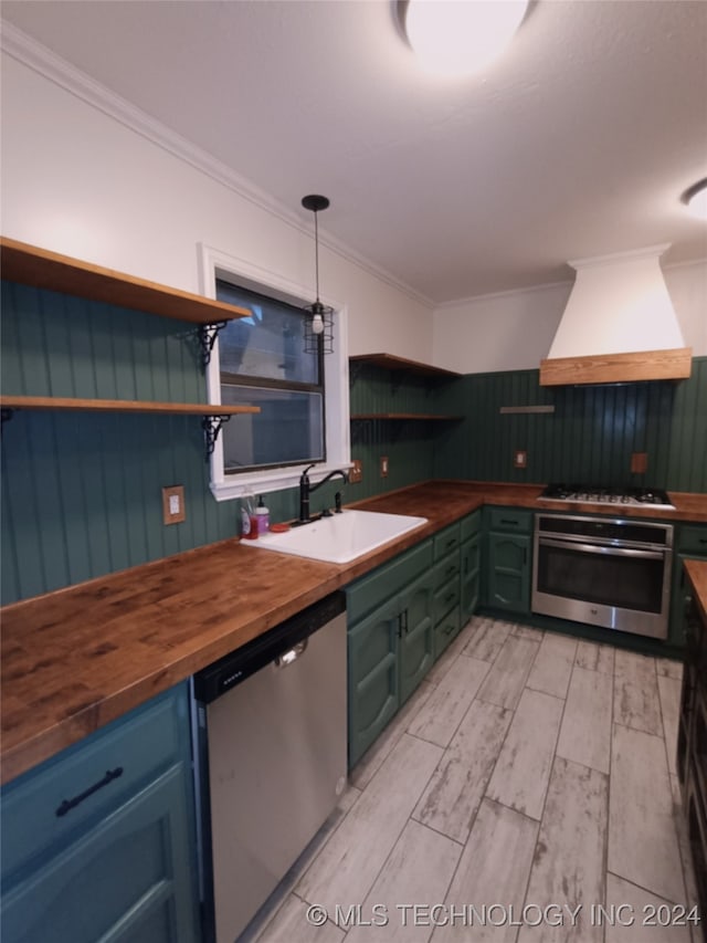 kitchen featuring butcher block counters, sink, stainless steel appliances, pendant lighting, and custom exhaust hood