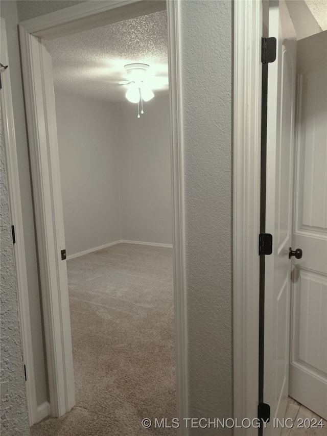 corridor featuring light carpet and a textured ceiling