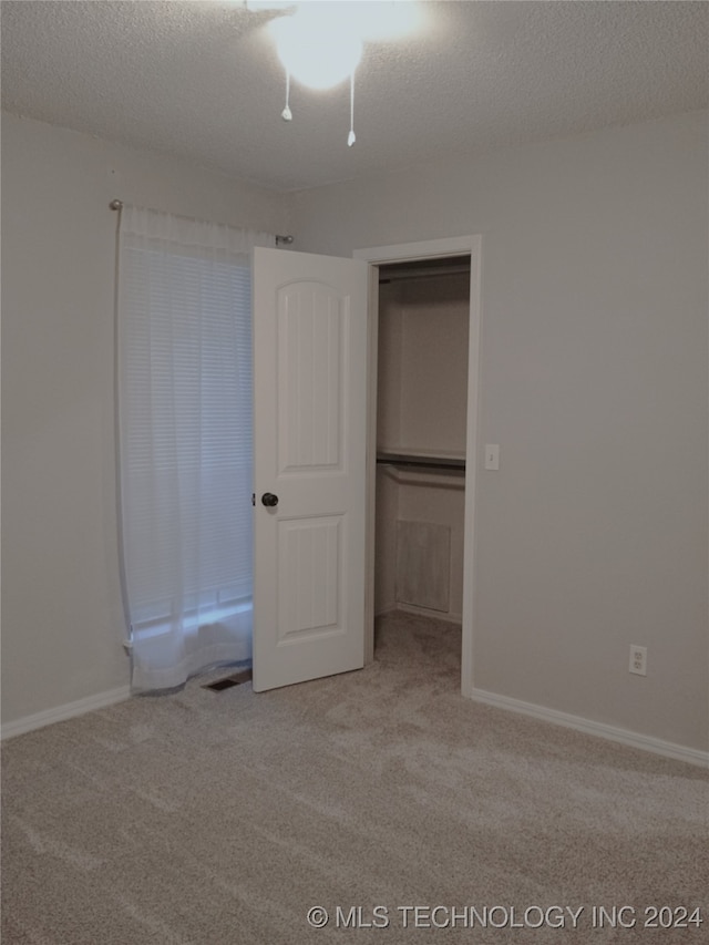 unfurnished bedroom with a closet, light colored carpet, and a textured ceiling