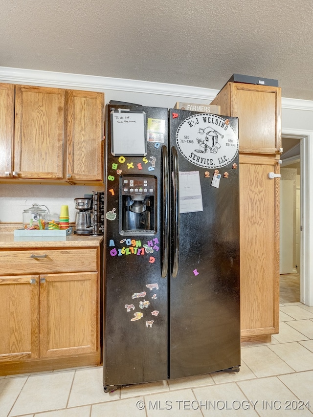 kitchen with a textured ceiling, light tile patterned flooring, black fridge, and crown molding