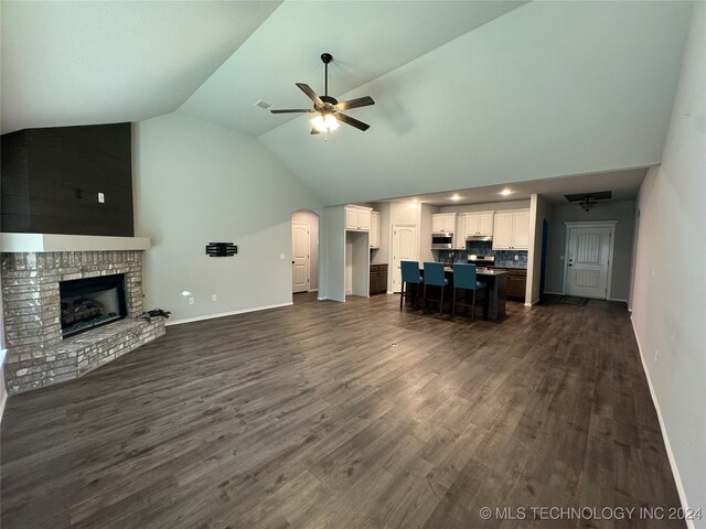 unfurnished living room with ceiling fan, a fireplace, lofted ceiling, and dark wood-type flooring