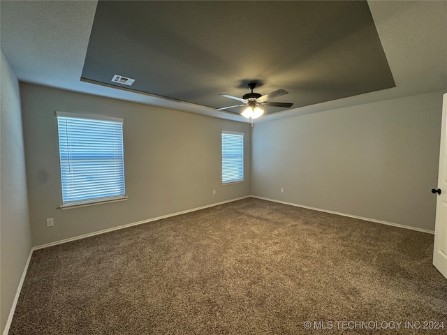 spare room with dark colored carpet, ceiling fan, and a raised ceiling