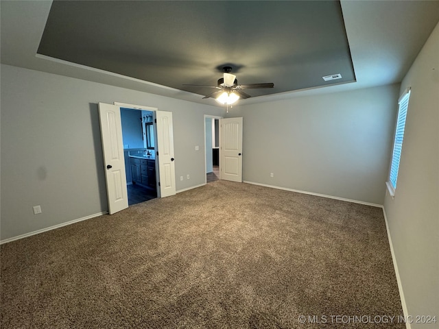 unfurnished bedroom featuring carpet flooring, ceiling fan, ensuite bathroom, and a tray ceiling