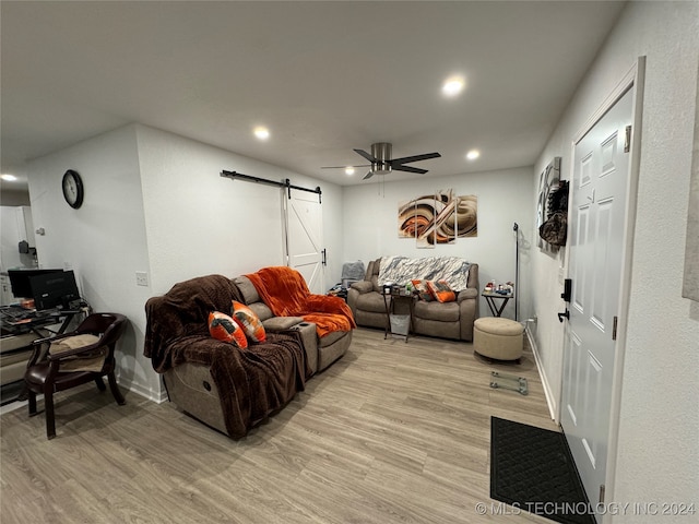 living room with ceiling fan, a barn door, and light hardwood / wood-style flooring