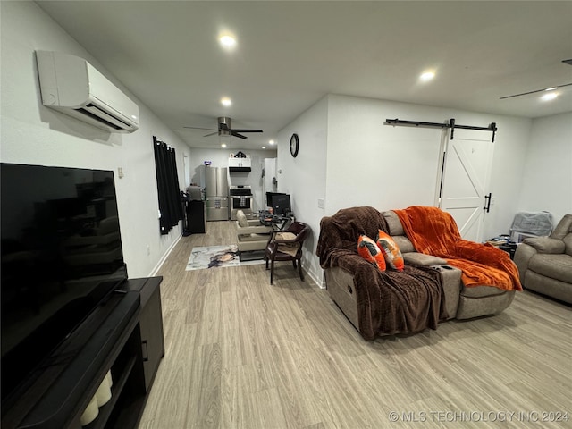 living room featuring light wood-type flooring, a barn door, a wall mounted AC, and ceiling fan