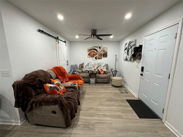 living room with ceiling fan, a barn door, and light wood-type flooring