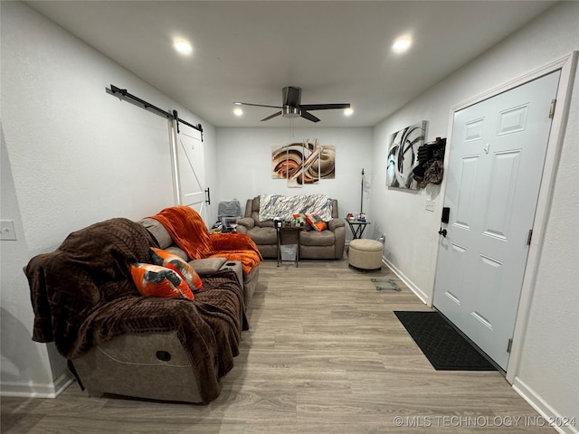 living room with a barn door, ceiling fan, and light wood-type flooring