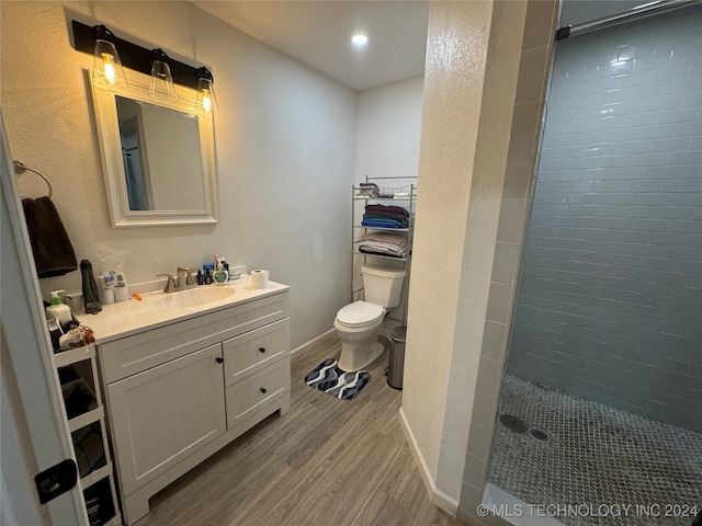 bathroom featuring a tile shower, toilet, vanity, and hardwood / wood-style flooring