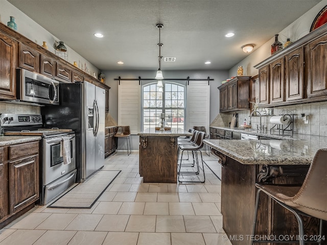 kitchen featuring dark brown cabinetry, a barn door, a breakfast bar, a kitchen island, and appliances with stainless steel finishes