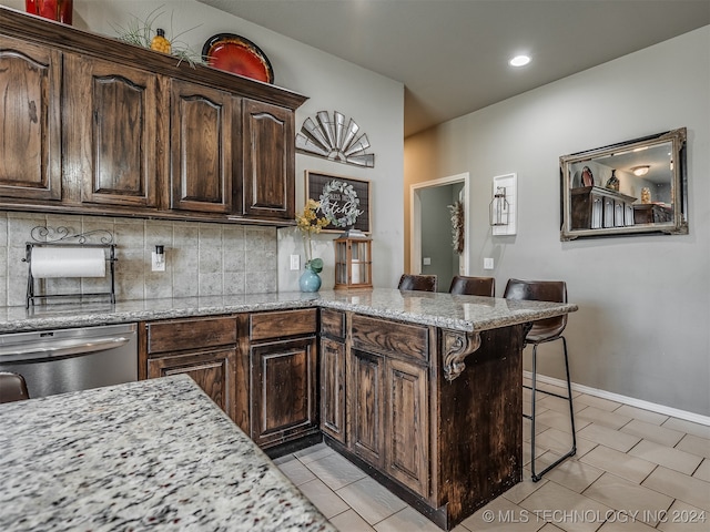 kitchen featuring a breakfast bar area, kitchen peninsula, light stone counters, and tasteful backsplash