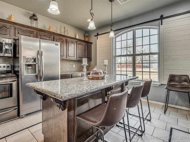 kitchen with backsplash, dark brown cabinets, stainless steel appliances, a barn door, and an island with sink