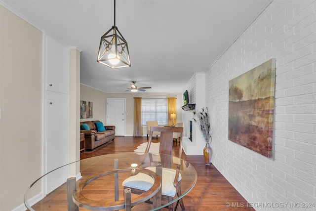 dining space featuring crown molding, dark hardwood / wood-style floors, ceiling fan, a fireplace, and brick wall