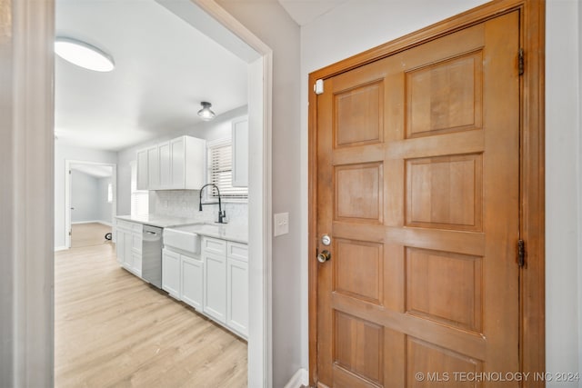 kitchen featuring backsplash, stainless steel dishwasher, sink, light hardwood / wood-style floors, and white cabinetry