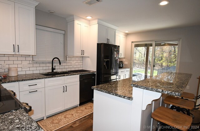 kitchen featuring black refrigerator with ice dispenser, a kitchen island, white cabinetry, and sink