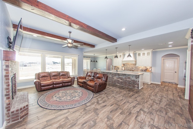 living room with hardwood / wood-style floors, crown molding, ceiling fan, a fireplace, and beamed ceiling